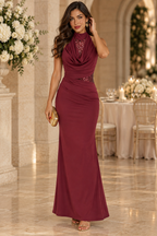 Vestido largo de fiesta granate de SXIA con cuello halter, escote drapeado y detalles de lentejuelas. Vista frontal de cuerpo entero de modelo con bolso dorado para invitada de boda.