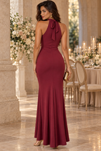Vista trasera del vestido largo granate de SXIA mostrando el cuello halter atado con lazo, espalda ajustada y caída fluida de la falda para evento de noche.
